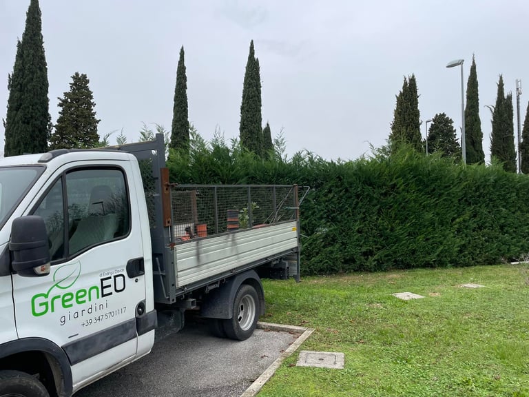 GreenED landscaping truck with open bed parked beside a manicured lawn and tall cypress hedge fence