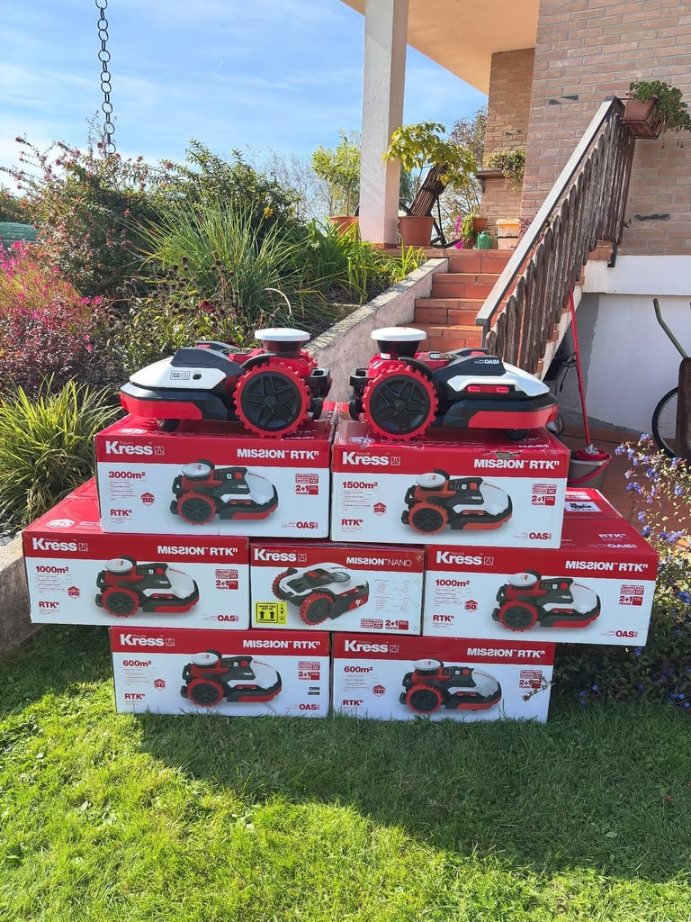 Stack of Kress robotic lawn mowers displayed in a garden with a patio and landscaping in the background