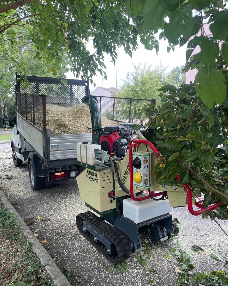 Small cream and red wood chipping machine on tracked base with loaded chip truck in background on tree-lined path